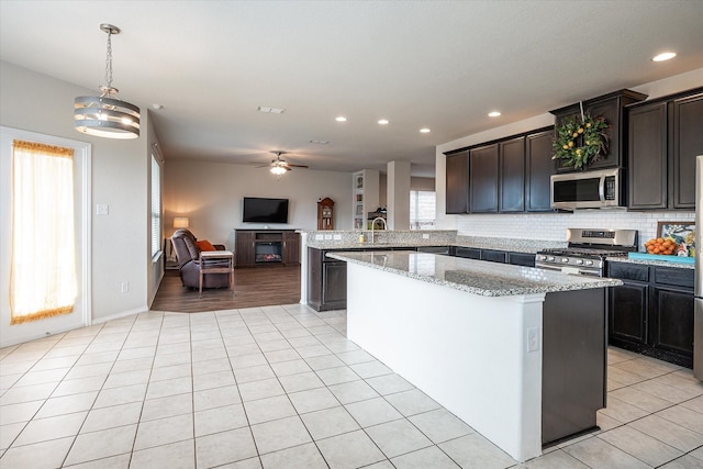 kitchen featuring pendant lighting, backsplash, ceiling fan with notable chandelier, sink, and stainless steel appliances