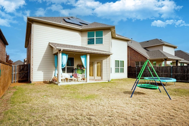 back of property with solar panels, a patio, a trampoline, and a yard