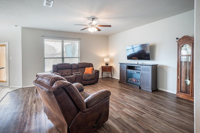 living room with ceiling fan, a fireplace, dark hardwood / wood-style flooring, and a textured ceiling