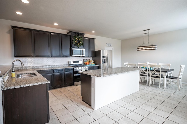 kitchen with light stone countertops, stainless steel appliances, sink, a center island, and hanging light fixtures