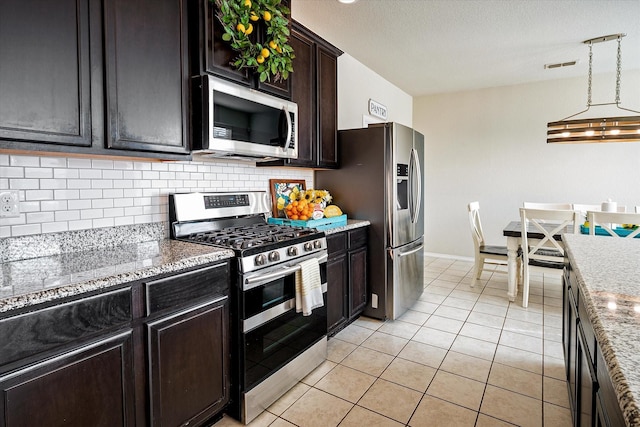 kitchen with dark brown cabinets, stainless steel appliances, light tile patterned floors, decorative light fixtures, and a notable chandelier