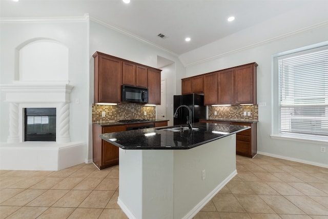 kitchen featuring a kitchen island with sink, sink, black appliances, light tile patterned floors, and dark stone countertops