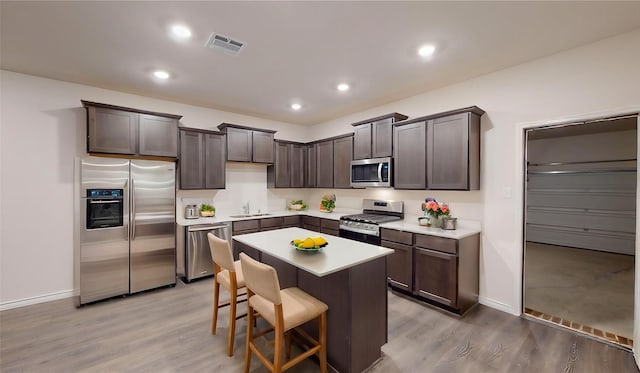 kitchen featuring a center island, sink, stainless steel appliances, a kitchen bar, and dark brown cabinets