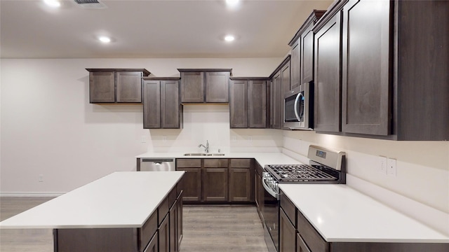 kitchen with appliances with stainless steel finishes, light wood-type flooring, dark brown cabinets, sink, and a center island