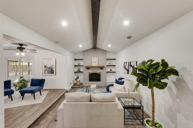 living room with ceiling fan, hardwood / wood-style floors, lofted ceiling with beams, and a brick fireplace