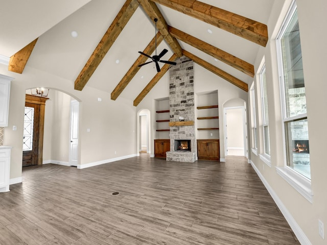 unfurnished living room featuring beamed ceiling, built in shelves, high vaulted ceiling, and a stone fireplace