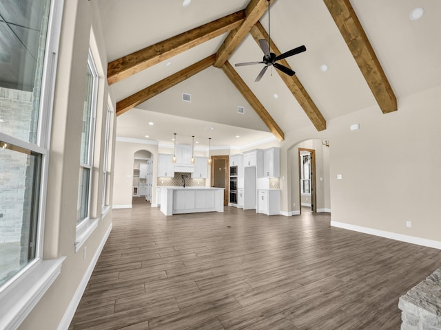 unfurnished living room with beamed ceiling, dark hardwood / wood-style floors, high vaulted ceiling, and ceiling fan