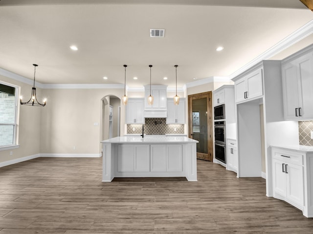 kitchen with a center island with sink, decorative light fixtures, white cabinetry, and custom exhaust hood