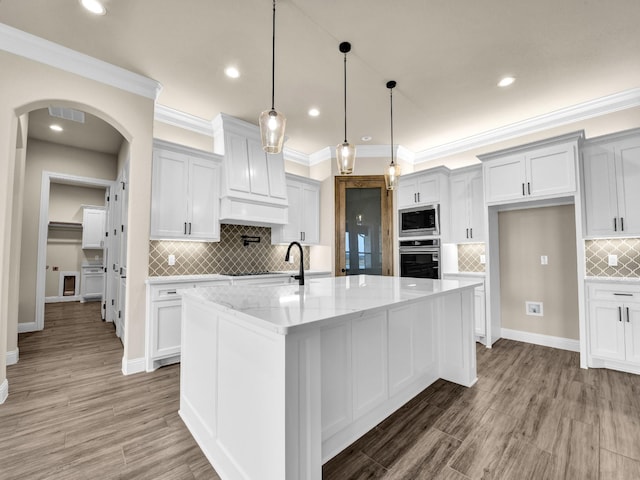 kitchen featuring light stone countertops, stainless steel appliances, a center island with sink, white cabinetry, and hanging light fixtures