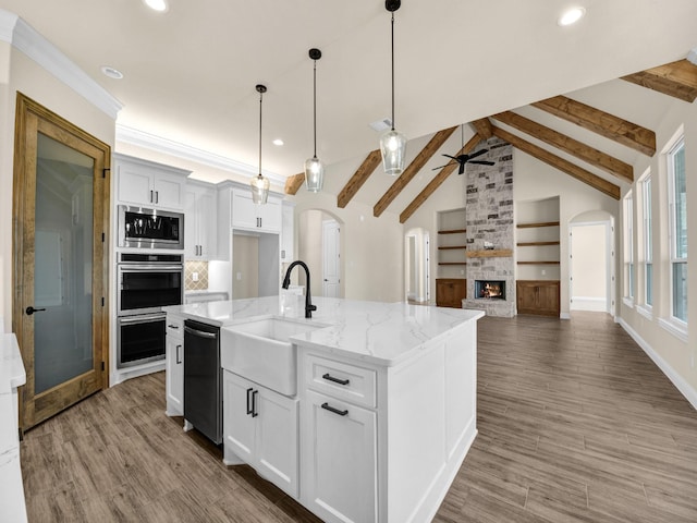 kitchen featuring a kitchen island with sink, white cabinets, a stone fireplace, sink, and stainless steel appliances