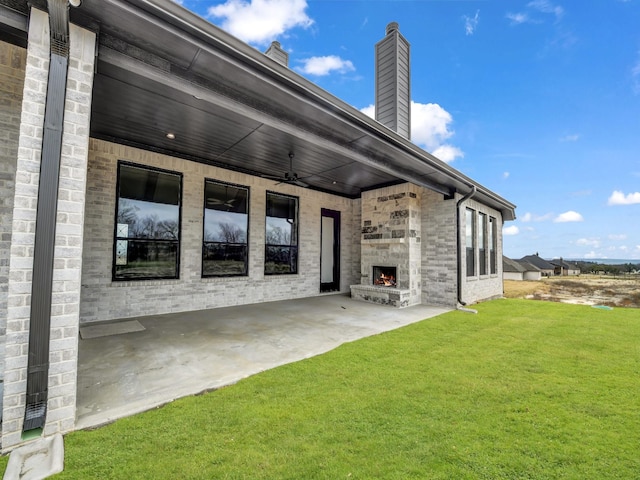 rear view of property featuring ceiling fan, a yard, and an outdoor stone fireplace