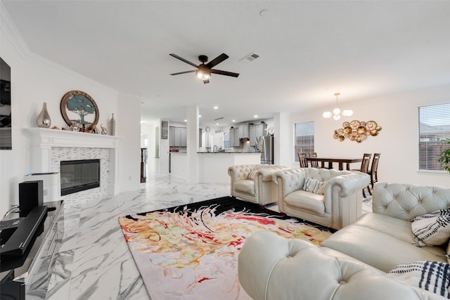 living room featuring ceiling fan with notable chandelier, ornamental molding, and a tile fireplace