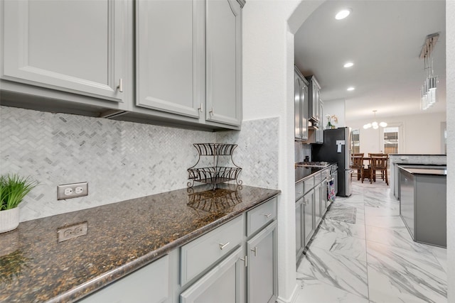 kitchen featuring dark stone counters, an inviting chandelier, hanging light fixtures, decorative backsplash, and gray cabinets