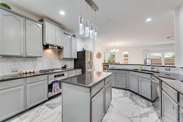 kitchen with appliances with stainless steel finishes, sink, decorative light fixtures, an inviting chandelier, and a kitchen island