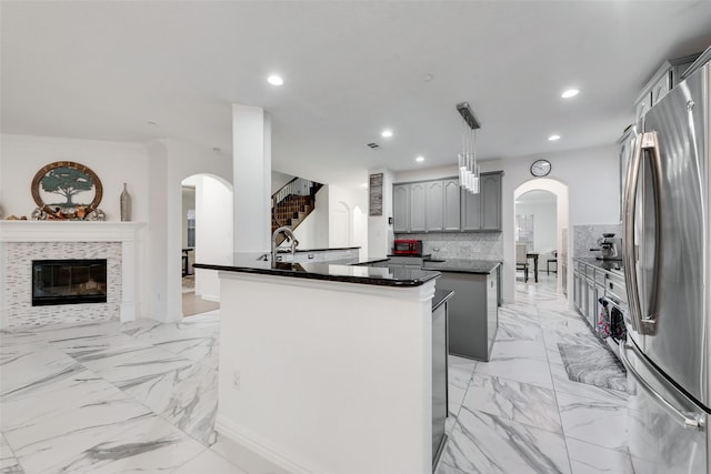 kitchen featuring a center island, gray cabinets, stainless steel fridge, tasteful backsplash, and a tiled fireplace