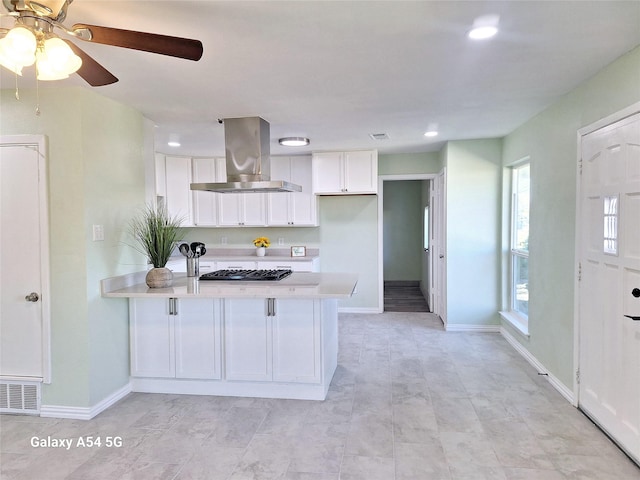 kitchen featuring stainless steel gas stovetop, island range hood, white cabinetry, and kitchen peninsula