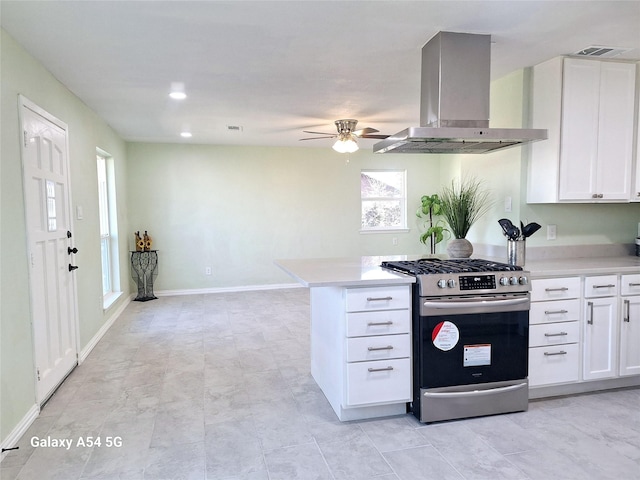 kitchen with white cabinetry, stainless steel gas range oven, wall chimney exhaust hood, and ceiling fan