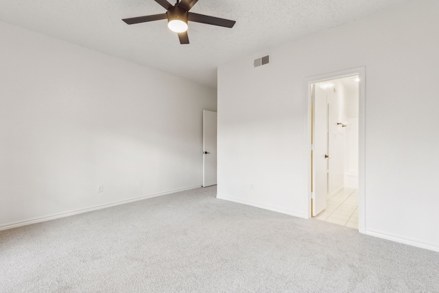 spare room with a textured ceiling, light colored carpet, and ceiling fan