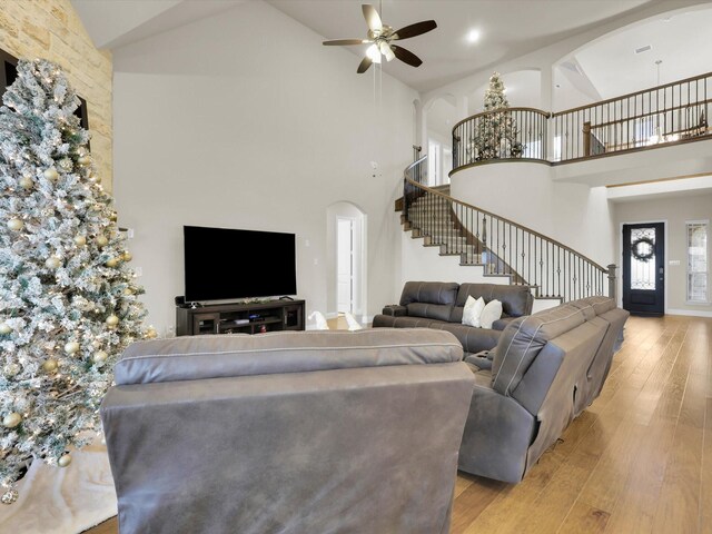 living area with light wood finished floors, ceiling fan, stairs, arched walkways, and high vaulted ceiling