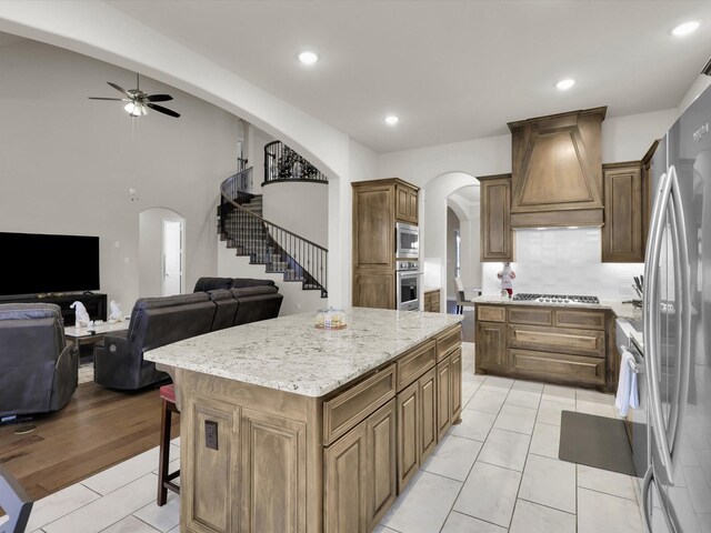 kitchen with light tile patterned flooring, a kitchen island, a stone fireplace, decorative light fixtures, and light stone counters