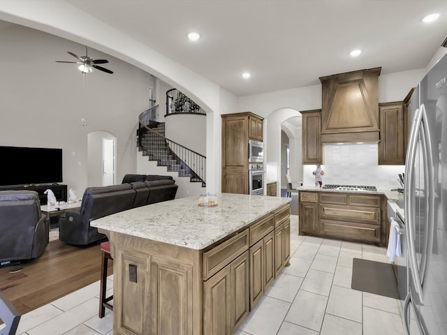 kitchen featuring arched walkways, ceiling fan, custom range hood, appliances with stainless steel finishes, and open floor plan