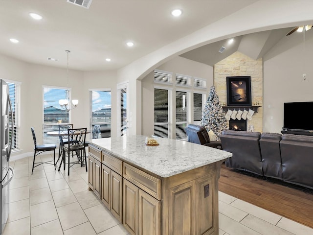 kitchen featuring light stone countertops, open floor plan, light tile patterned floors, a stone fireplace, and a notable chandelier