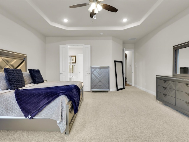 carpeted bedroom with ensuite bath, a raised ceiling, and ceiling fan