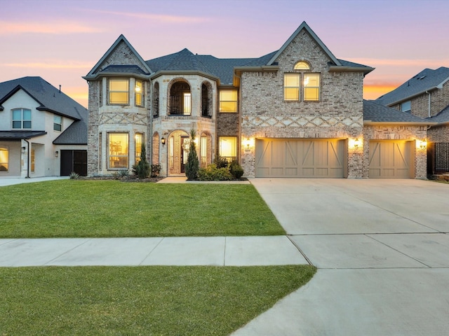 french provincial home with a front yard, concrete driveway, and brick siding