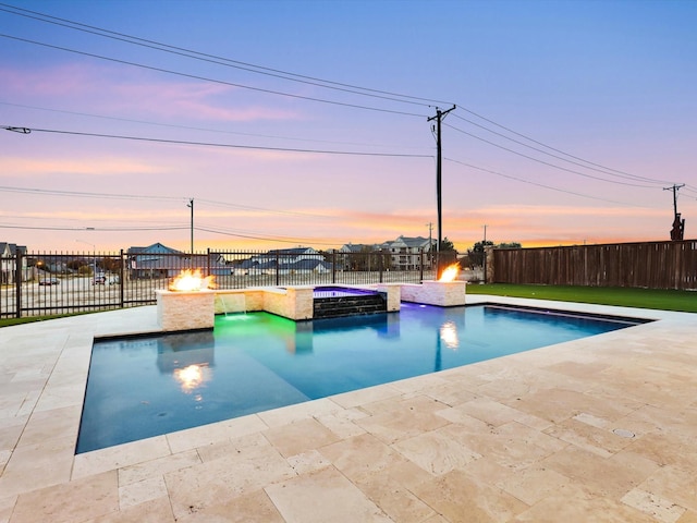 pool at dusk featuring an in ground hot tub, an outdoor fire pit, and a patio