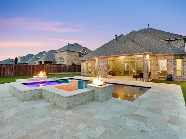 pool at dusk featuring an in ground hot tub, a patio area, and a fire pit