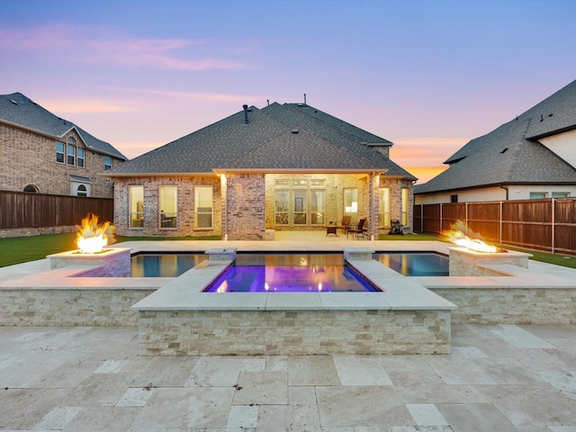 pool at dusk with a fire pit, a patio, and an in ground hot tub