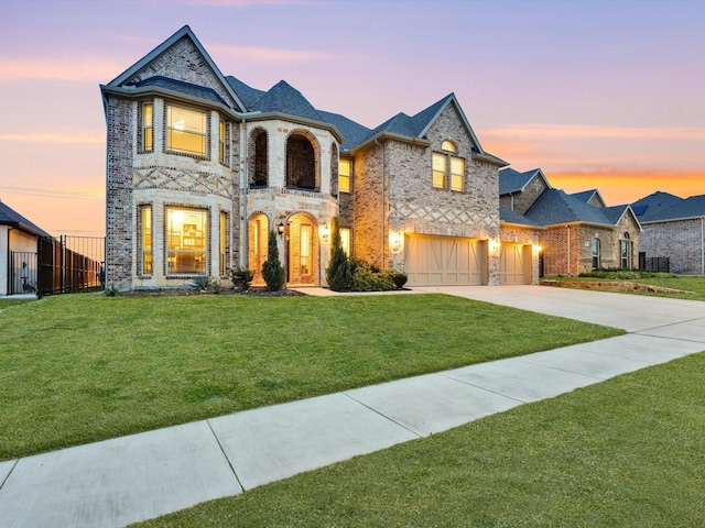 french provincial home featuring driveway, stone siding, fence, a yard, and a garage
