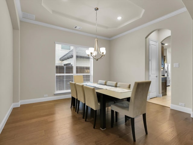 dining space with a notable chandelier, visible vents, a tray ceiling, and wood finished floors