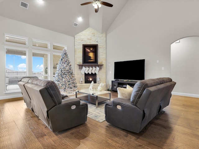 living room with hardwood / wood-style flooring, ceiling fan, a stone fireplace, and high vaulted ceiling