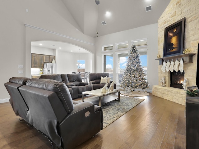 living room featuring a stone fireplace, dark wood-type flooring, and high vaulted ceiling