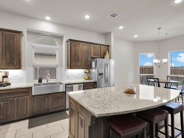 kitchen featuring light stone counters, visible vents, a sink, stainless steel appliances, and a kitchen bar
