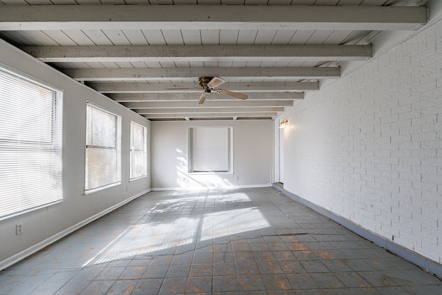 unfurnished room featuring beamed ceiling, a wealth of natural light, ceiling fan, and brick wall