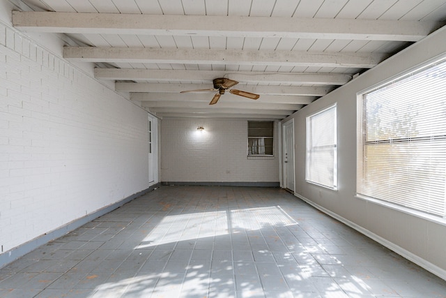 spare room with beam ceiling, ceiling fan, plenty of natural light, and brick wall