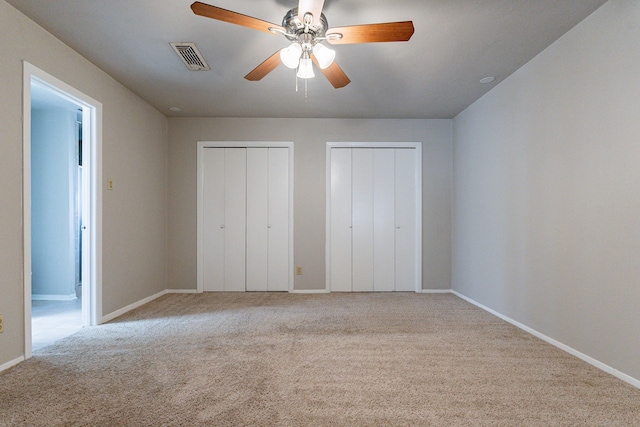 unfurnished bedroom with ceiling fan, light colored carpet, and two closets