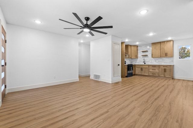 unfurnished living room with ceiling fan, sink, and light wood-type flooring