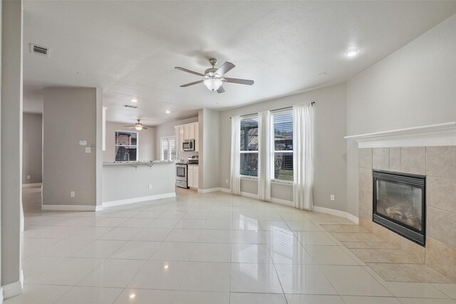 unfurnished living room featuring a tiled fireplace, ceiling fan, and light tile patterned floors