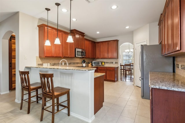 kitchen with pendant lighting, appliances with stainless steel finishes, kitchen peninsula, and light stone counters