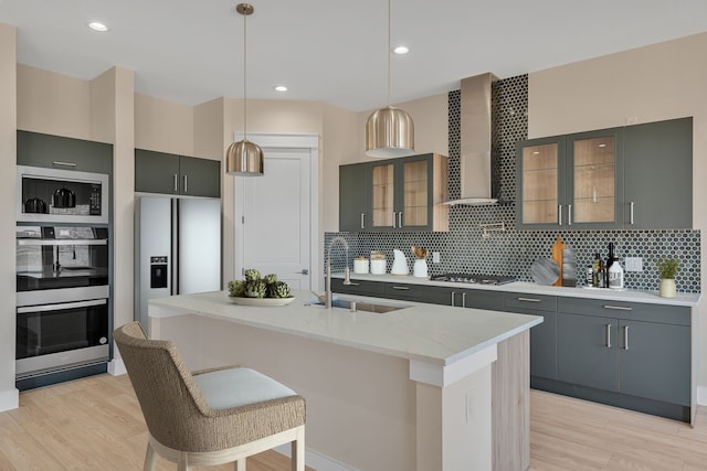 kitchen with light wood-style flooring, decorative backsplash, appliances with stainless steel finishes, a sink, and wall chimney exhaust hood