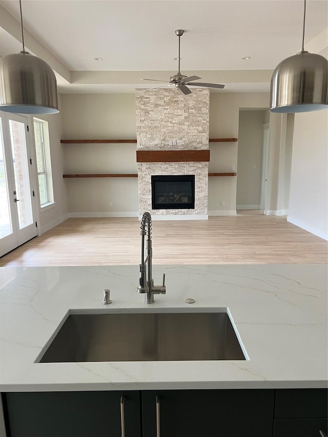 kitchen with sink, hanging light fixtures, a stone fireplace, light stone counters, and built in features