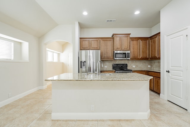 kitchen featuring backsplash, sink, an island with sink, appliances with stainless steel finishes, and light stone counters