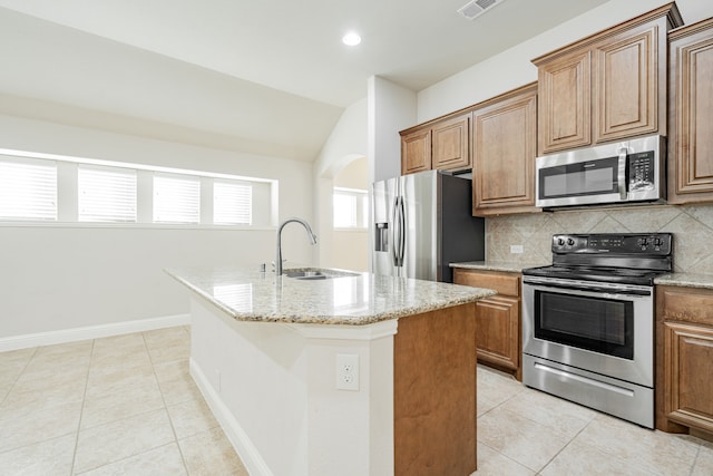 kitchen featuring sink, vaulted ceiling, light stone countertops, an island with sink, and stainless steel appliances