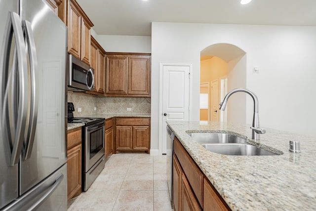 kitchen with light stone countertops, appliances with stainless steel finishes, decorative backsplash, sink, and light tile patterned floors