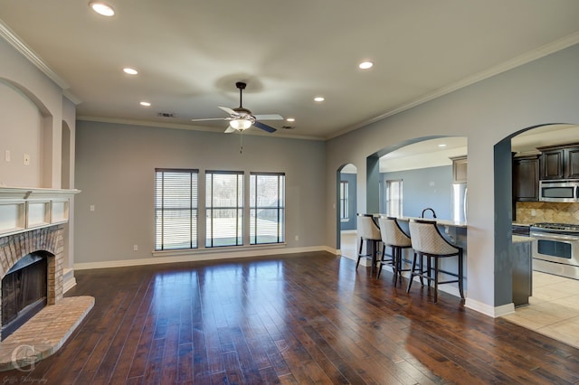 living room featuring hardwood / wood-style flooring, crown molding, a brick fireplace, and ceiling fan