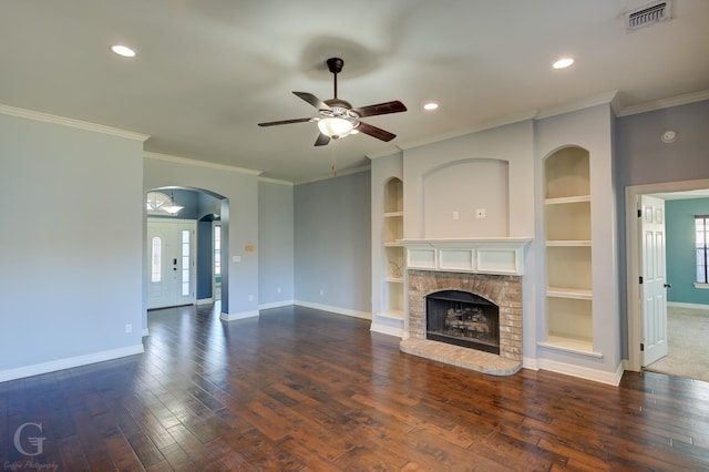 unfurnished living room featuring crown molding, built in shelves, ceiling fan, a fireplace, and dark hardwood / wood-style flooring