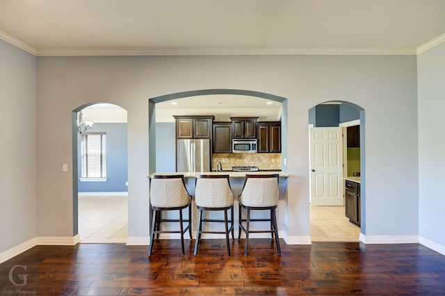 kitchen with dark wood-type flooring, a kitchen breakfast bar, ornamental molding, appliances with stainless steel finishes, and tasteful backsplash